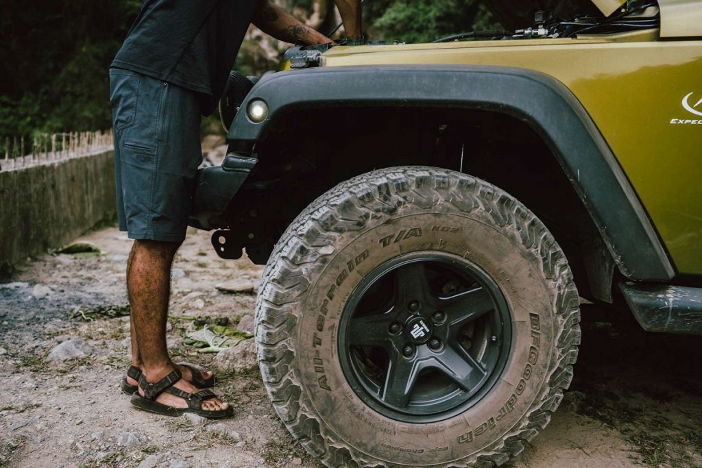 man standing in front of vehicle with huge tire covered in mud