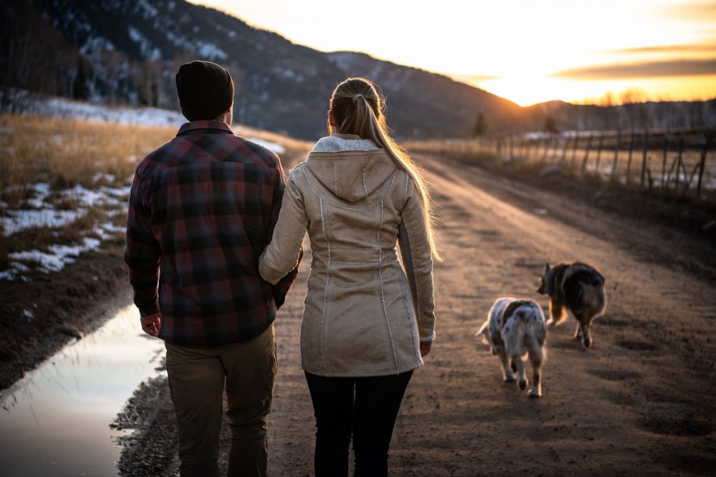 man in K&Uuml;HL plaid shirt and woman in K&Uuml;HL trench walking outdoors with two dogs