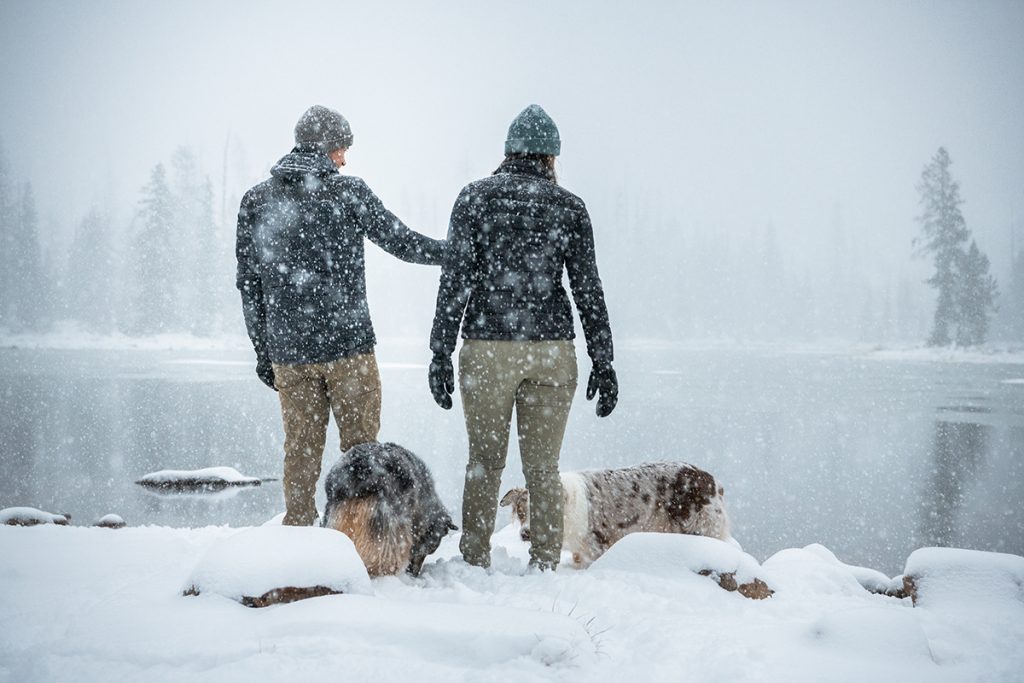 people in K&Uuml;HL clothing next to two dogs on snowy field